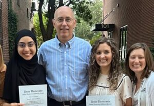 four men and women smiling and holding diplomas